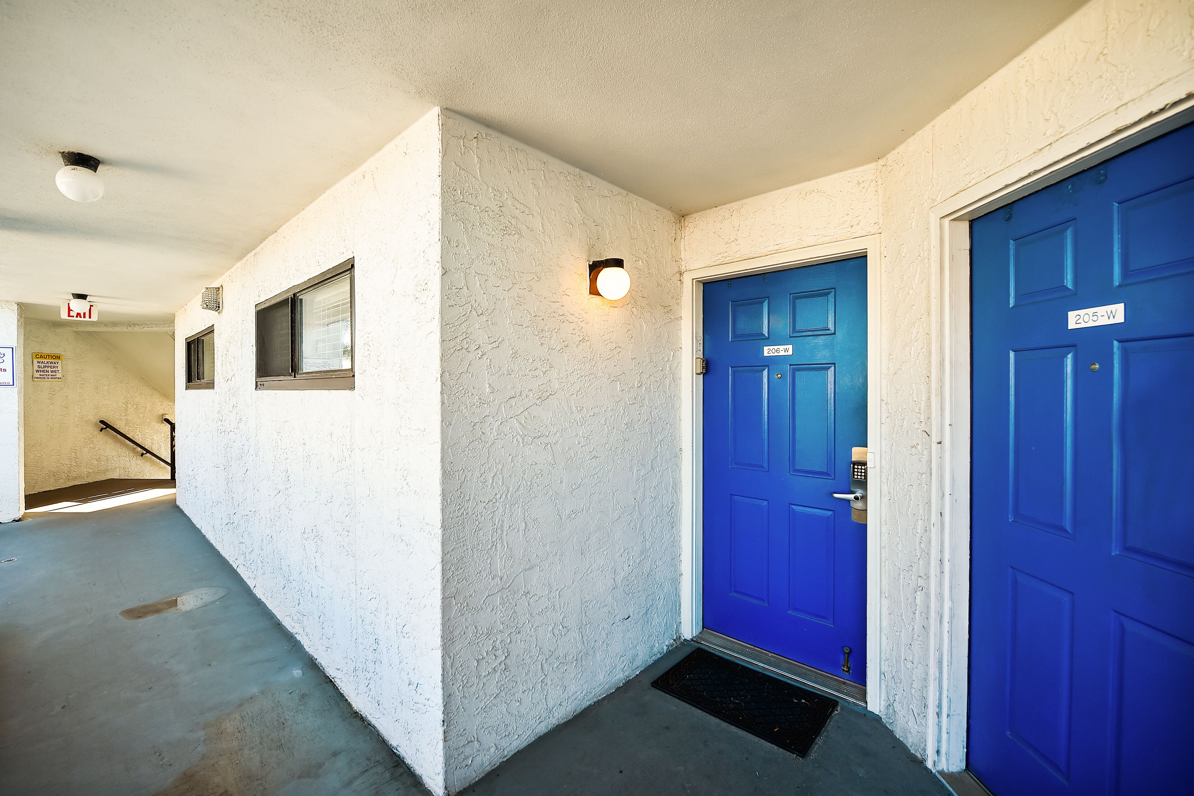 Un pasillo con una puerta azul identificada con '206-W' y una puerta blanca con la etiqueta '205-W'.