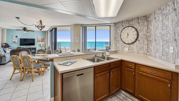 A modern kitchen with a dishwasher, wooden cabinets, and a large window overlooking the ocean.