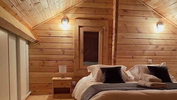 A cozy attic bedroom with a wooden sloped ceiling, a bed with pillows, a nightstand, and a fluffy rug. - Le Familial 4* - SPA & SAUNA - 6 people (Rochesson)