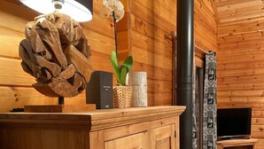 A wooden cabin interior with a central fireplace, wooden cabinets, and a television. - Le Familial 4* - SPA & SAUNA - 6 people (Rochesson)