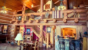 A rustic cabin interior with a wooden staircase, a dining area, and a bar. - Beautiful Log Cabin w/ Beachfront & Stunning Lake Views in Coeur d'Alene Idaho. (Harrison)