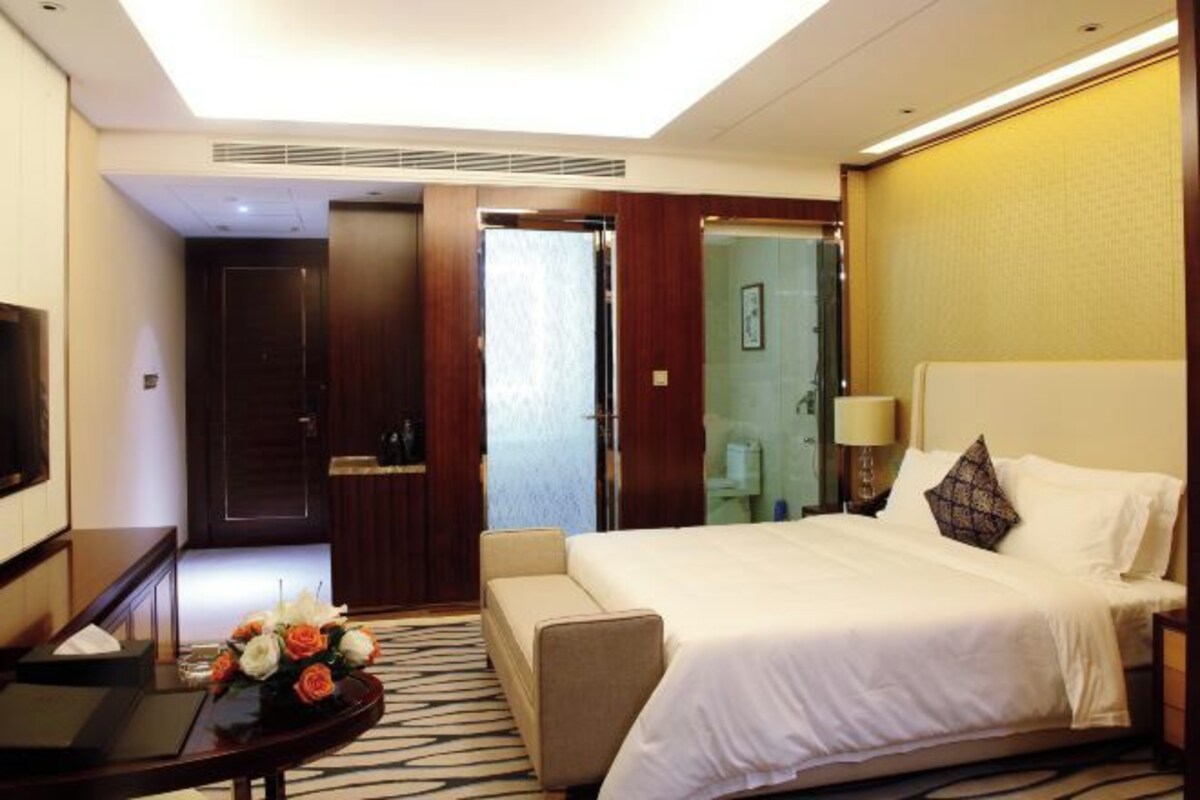 Habitación de hotel con cama, escritorio, silla, televisor y un arreglo floral.