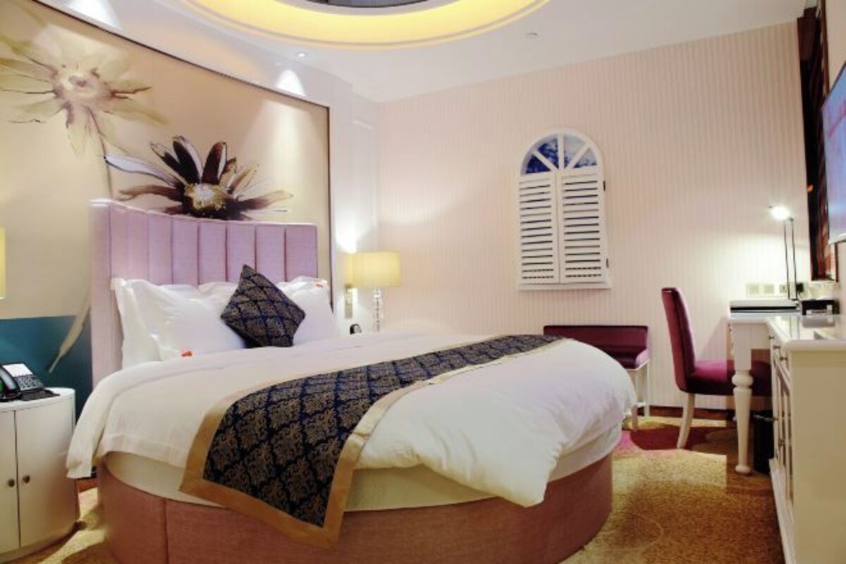 Una habitación de hotel con una cama grande, un escritorio con silla, una ventana con contraventanas y un adorno en la pared.