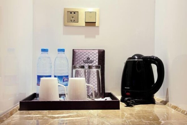 Habitación de hotel con cafetera, dos botellas de agua y una bandeja con tazas y una vela.