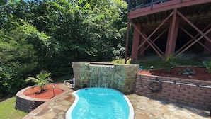 A swimming pool with a stone border, surrounded by a brick wall and a stone waterfall feature. - Rivers Bend Cabin, Stunning Caddo River & Ouachita Mountain Views (Amity)