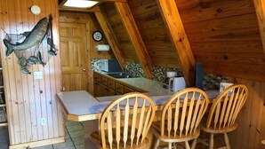 A wooden cabin with a kitchen area, a dining table with chairs, and a fish display on the wall. - Rivers Bend Cabin, Stunning Caddo River & Ouachita Mountain Views (Amity)