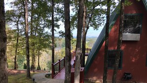 A wooden deck leading to a red building surrounded by tall trees. - Rivers Bend Cabin, Stunning Caddo River & Ouachita Mountain Views (Amity)