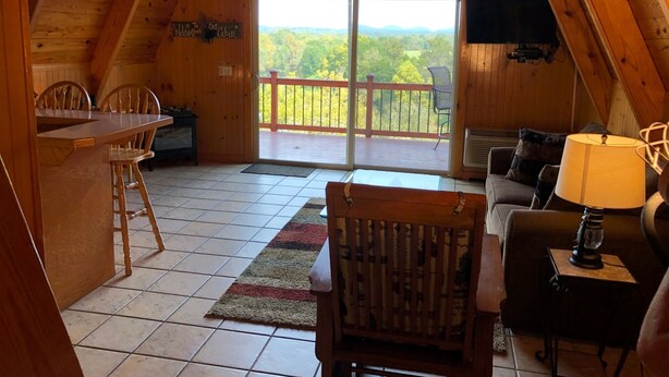 A cozy cabin with a wooden interior, a dining area, a sofa, and a balcony with a view of the forest. - Rivers Bend Cabin, Stunning Caddo River & Ouachita Mountain Views (Amity)