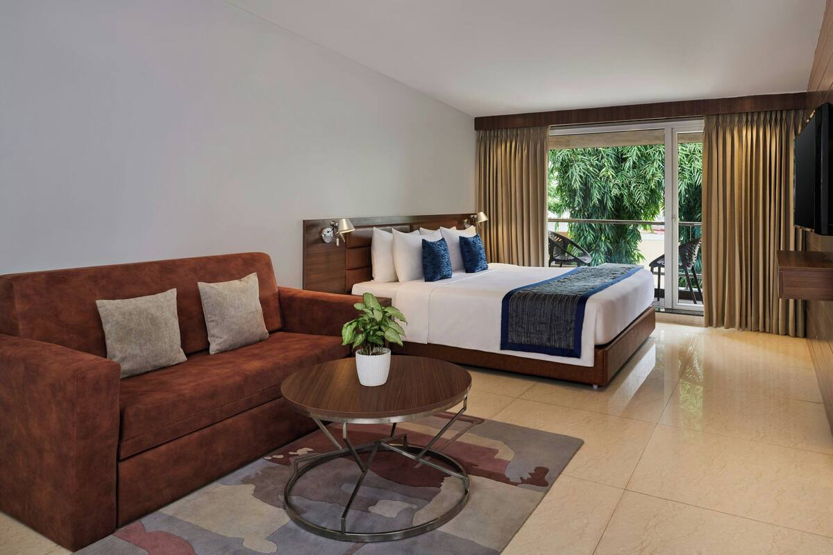 Ein Hotelzimmer mit einem Bett, einer braunen Couch, einem kleinen runden Tisch und einer Zimmerpflanze.