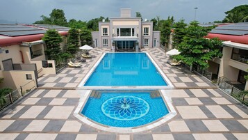 A swimming pool with a geometric tile pattern, surrounded by a checkered floor and shaded by umbrellas.