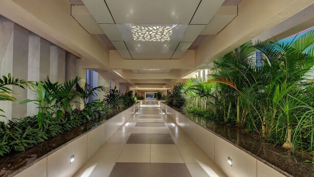A corridor with a tiled floor, green plants on both sides, and a patterned ceiling light. - The Fern Sardar Sarovar Resort, Series by Marriott (Garudeshwar)