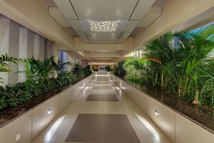 A corridor with a tiled floor, green plants on both sides, and a patterned ceiling light.