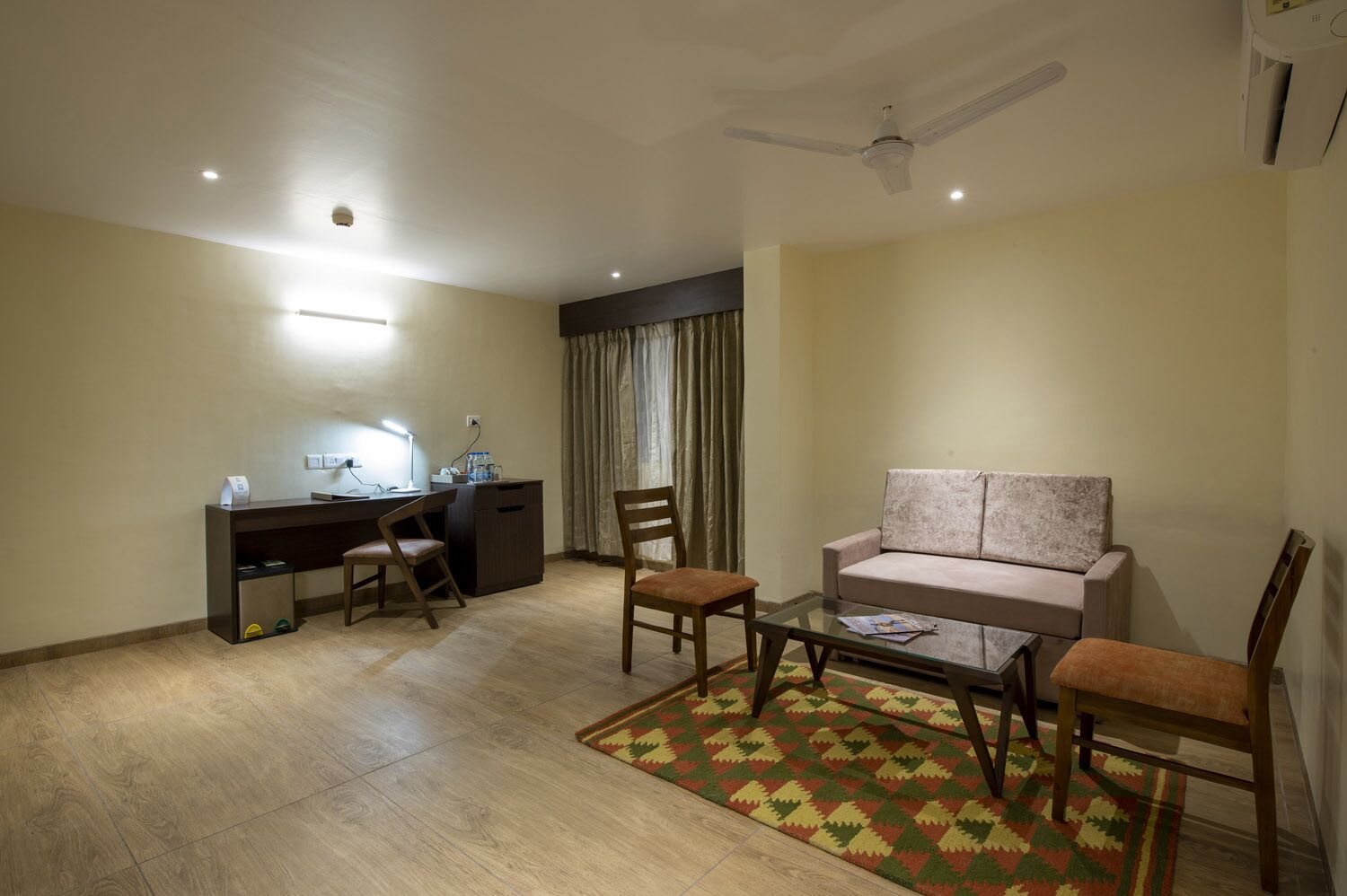 Una habitación de hotel con escritorio, sofá, mesa de centro y ventilador de techo.