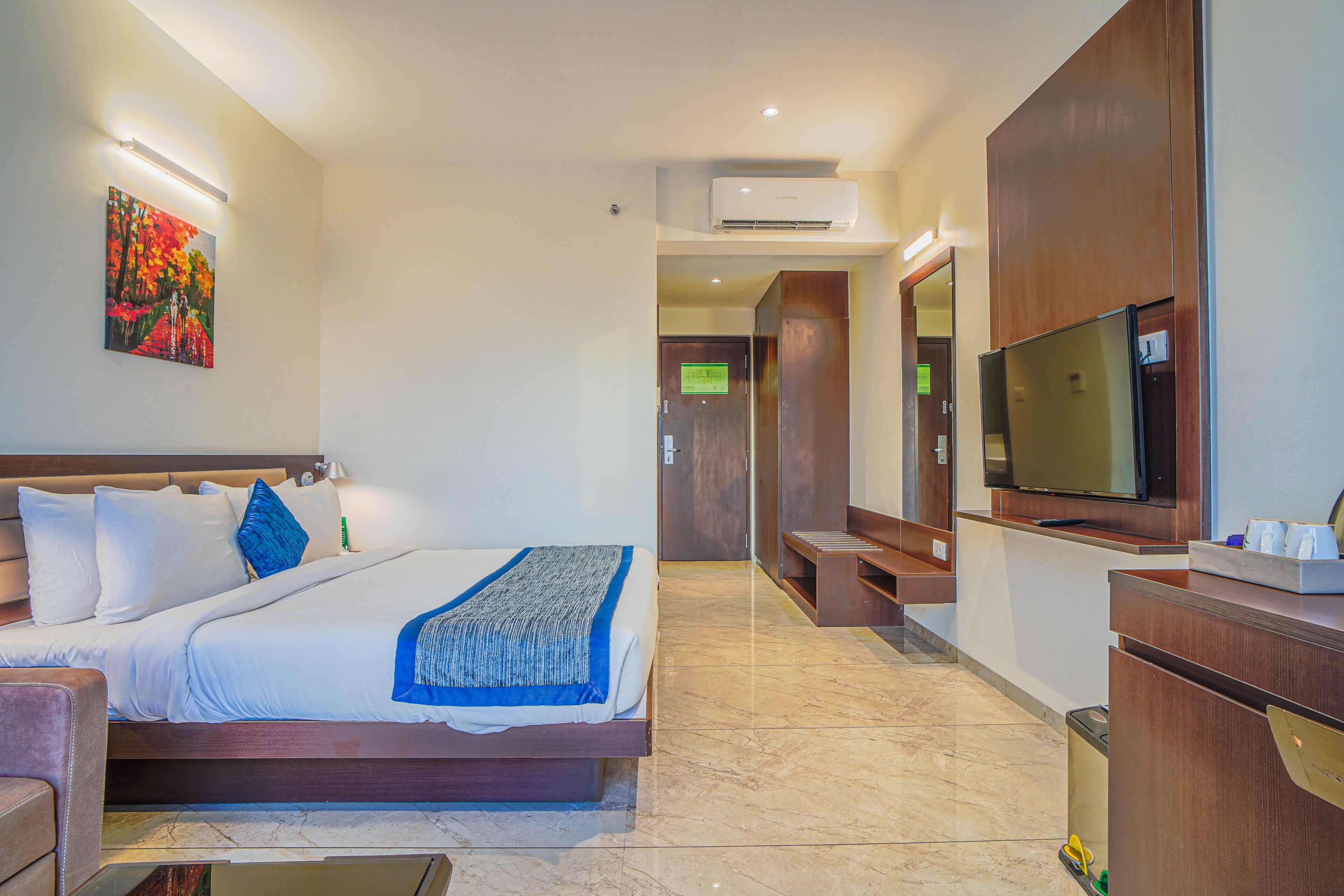 Habitación de hotel con una cama, televisión, escritorio y un cuadro en la pared.