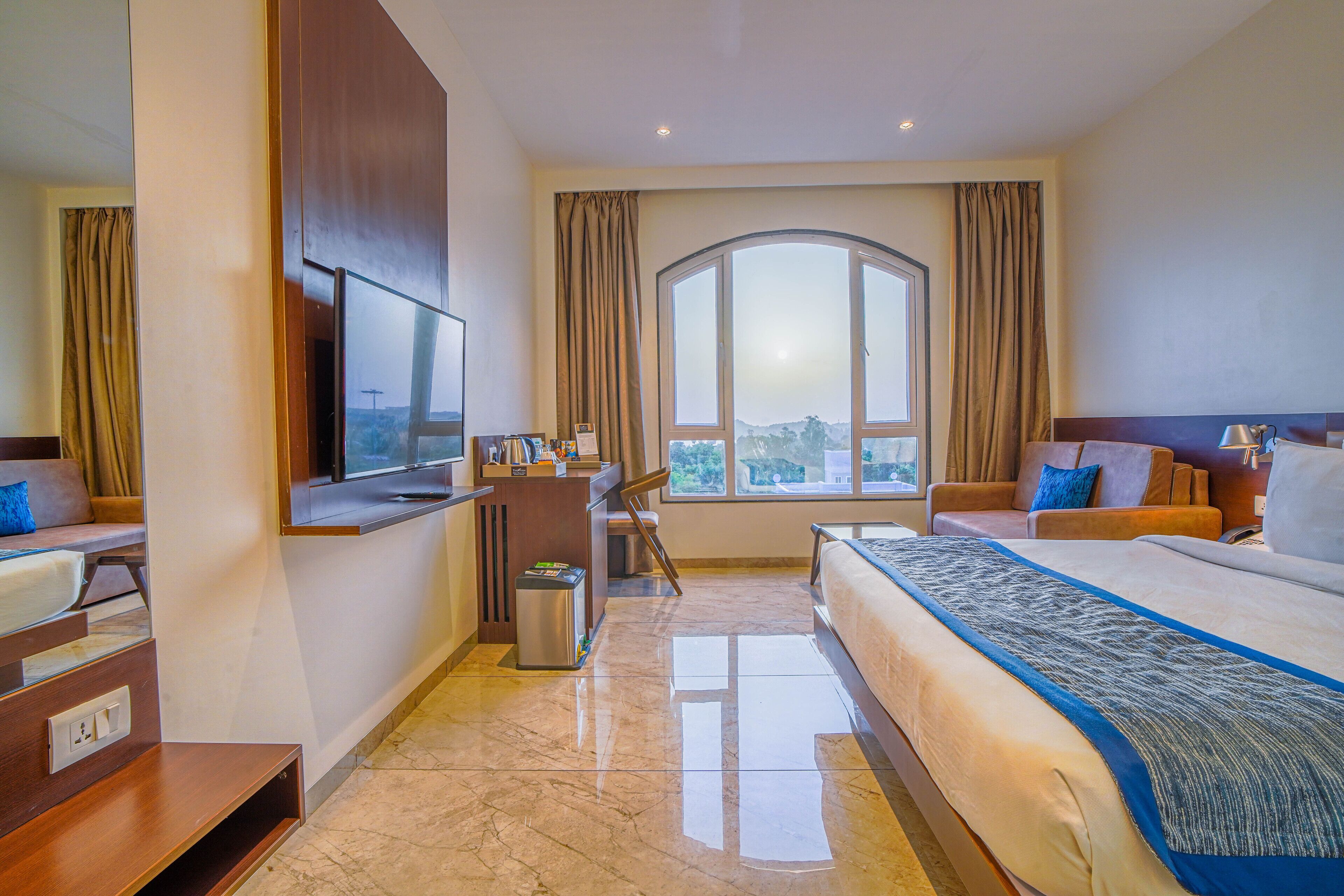 Ein Hotelzimmer mit einem großen Bett, einem Schreibtisch, einem Fernseher und Blick ins Freie.