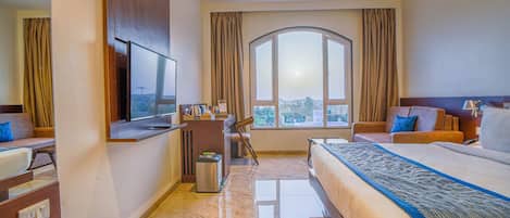 Ein Hotelzimmer mit einem großen Bett, einem Schreibtisch, einem Fernseher und Blick ins Freie.