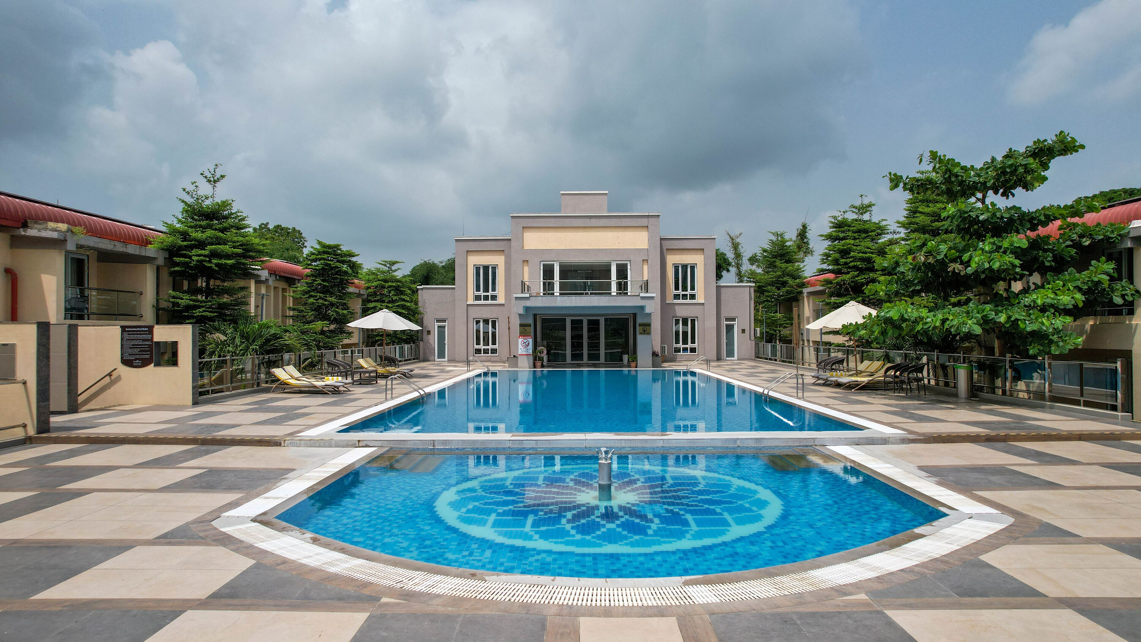 A swimming pool with a geometric tile pattern, surrounded by lounge chairs and umbrellas, with a building in the background.