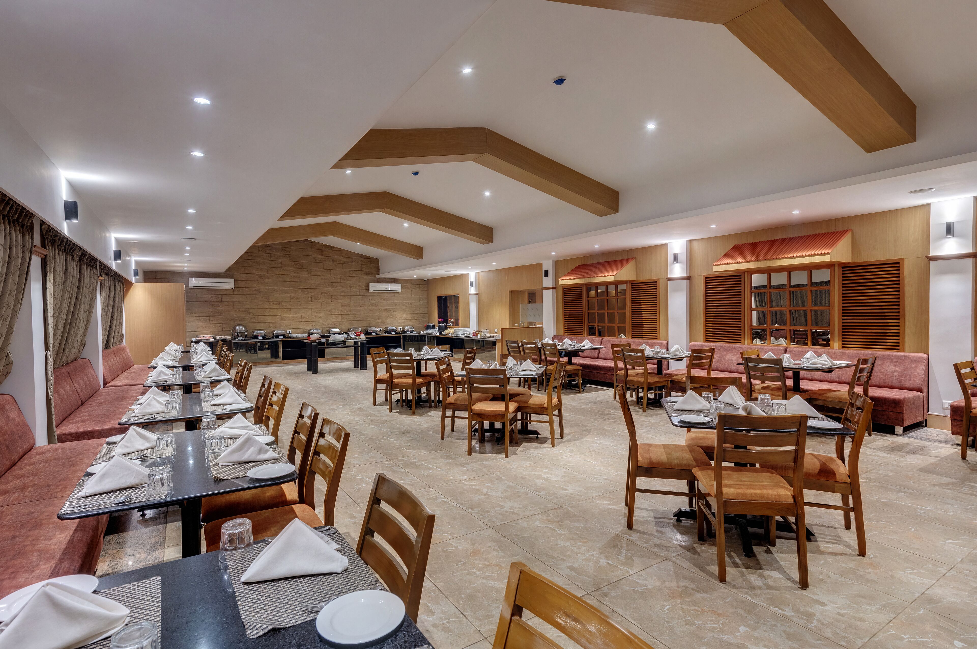 A spacious dining area with multiple tables and chairs, a brick wall, and wooden ceiling beams.