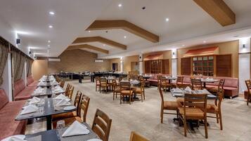 A spacious dining area with multiple tables and chairs, a brick wall, and wooden ceiling beams.