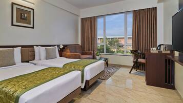 A hotel room with two beds, a desk, a chair, a television, and a large window with curtains.