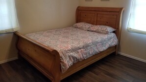 Una cama de madera con colcha y almohadas estampadas, un cabecero de madera y dos letreros decorativos en la pared.
