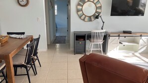 A living room with a brown leather sofa, a wooden dining table with chairs, a TV, and a desk with a chair. - SHORT WALK TO VILLAGE, BEACH - HEATED POOL - LUSH LANDSCAPING.
TWO UNITS. (Siesta Key)