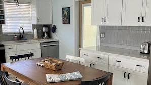 A modern kitchen with white cabinets, a wooden dining table, and black chairs. - SHORT WALK TO VILLAGE, BEACH - HEATED POOL - LUSH LANDSCAPING.
TWO UNITS. (Siesta Key)