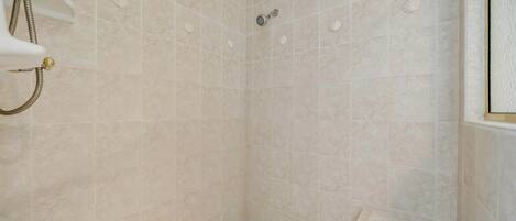 A shower with beige tiles and a handheld showerhead.