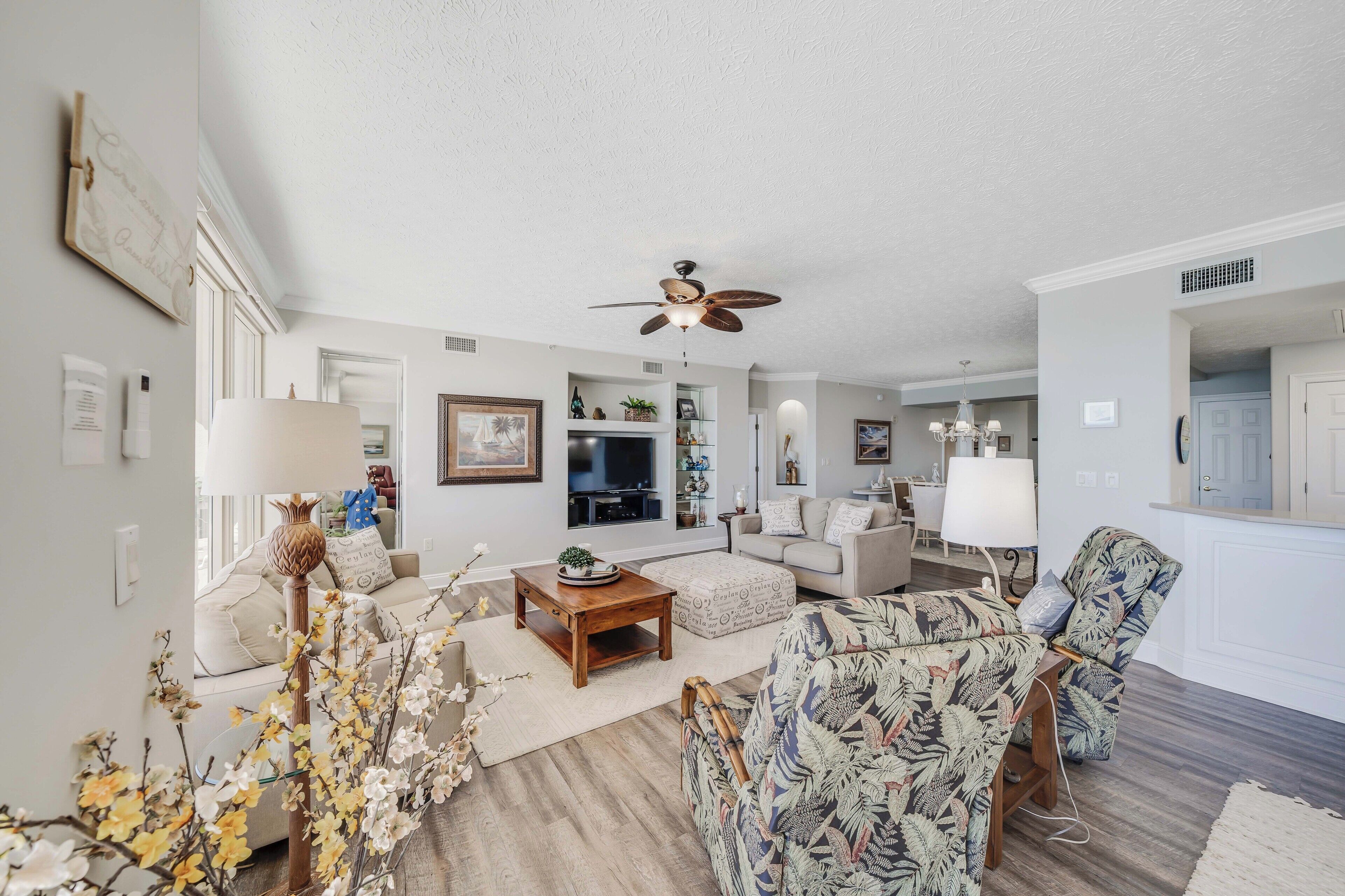 A spacious living room with a ceiling fan, a coffee table, a sofa, and a patterned armchair.