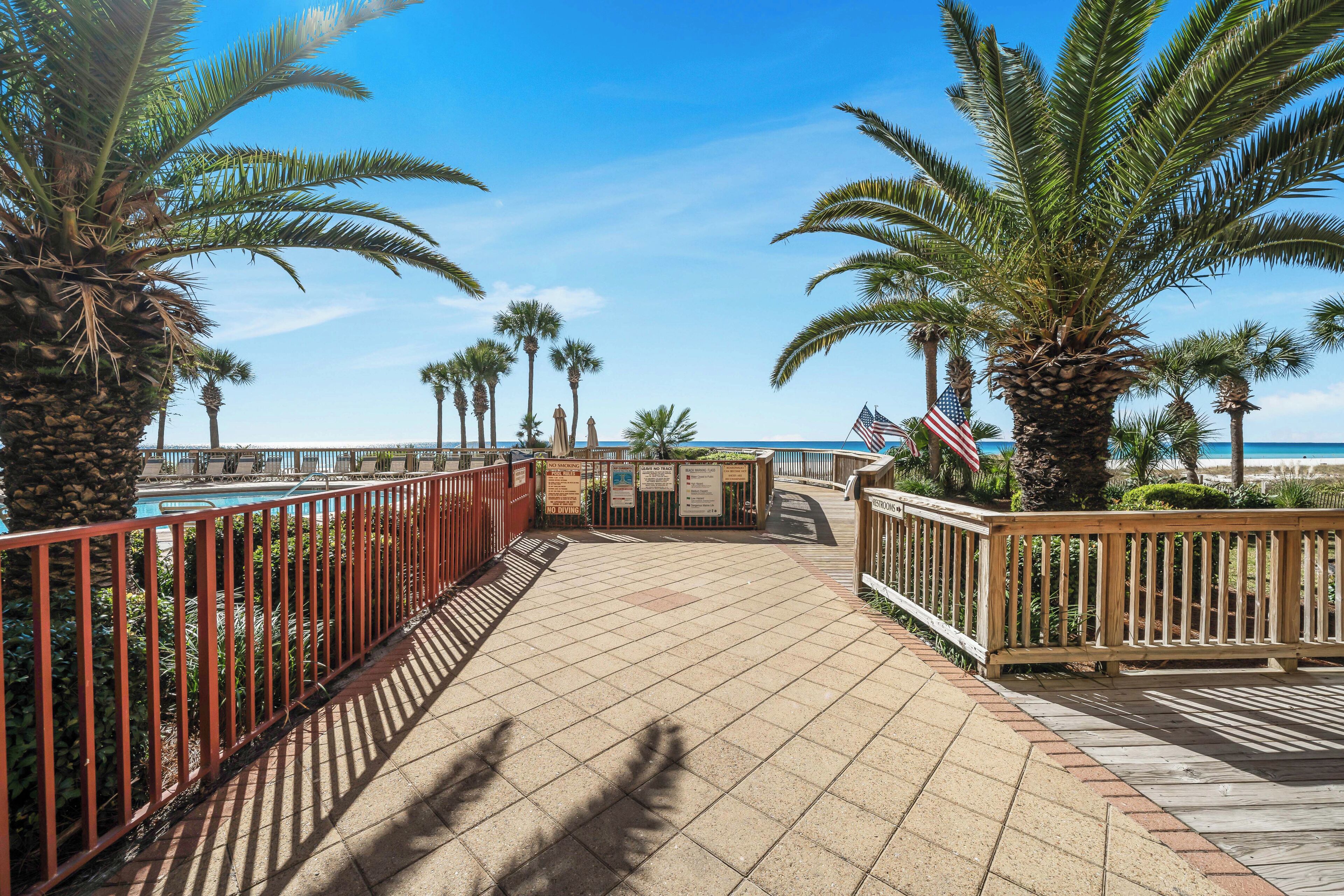 A paved deck with palm trees, a pool, and a wooden railing.