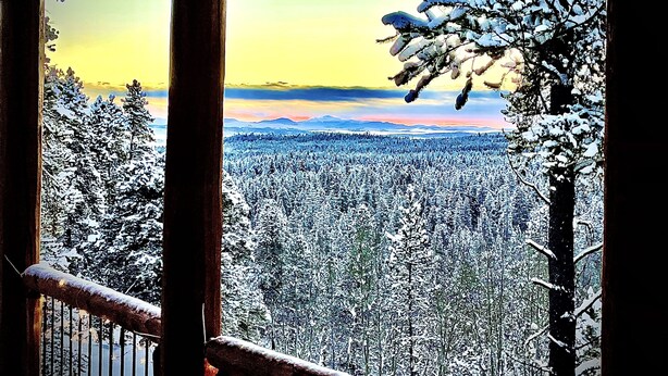 A snowy landscape with a mountain range in the distance, viewed from a wooden balcony.