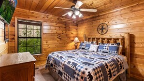 Ein Schlafzimmer in einer Holzhütte mit einem Bett, einem Deckenventilator, einem Fenster und einer Wanduhr.