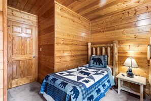A wooden cabin room with a bed, a nightstand, a lamp, and a door.