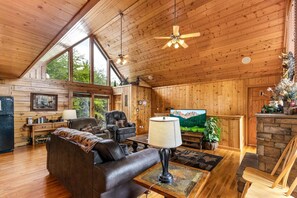 A cozy cabin interior with a fireplace, leather sofa, and a television.