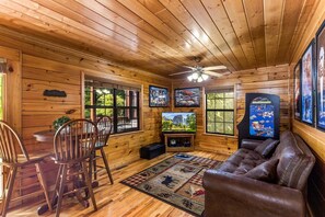 A wooden cabin interior with a dining area, a sofa, a ceiling fan, and framed pictures on the walls.