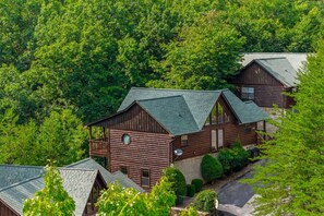 A log cabin with a balcony, surrounded by dense forest.