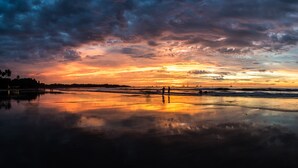 En strand vid solnedgången, med ett lugnt hav och en molnig himmel.
