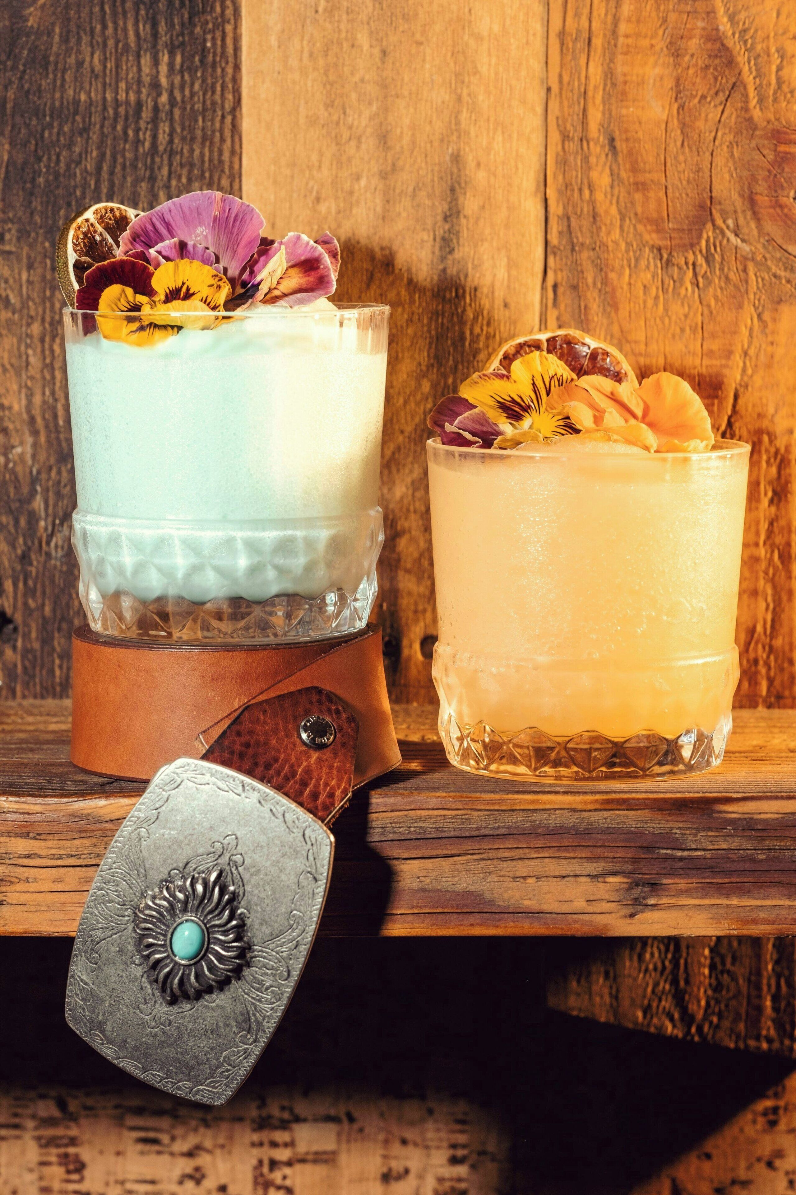 Deux verres remplis d’une boisson crémeuse, décorés de fleurs séchées, posés sur une surface en bois.
