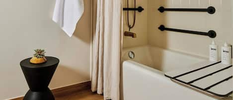 A modern bathroom with a bathtub, a shower with a rain showerhead, a towel rack, and a small side table with a plant.