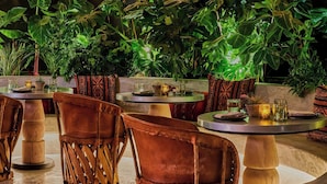 A restaurant interior with wicker hanging lamps, round tables, and cushioned chairs.