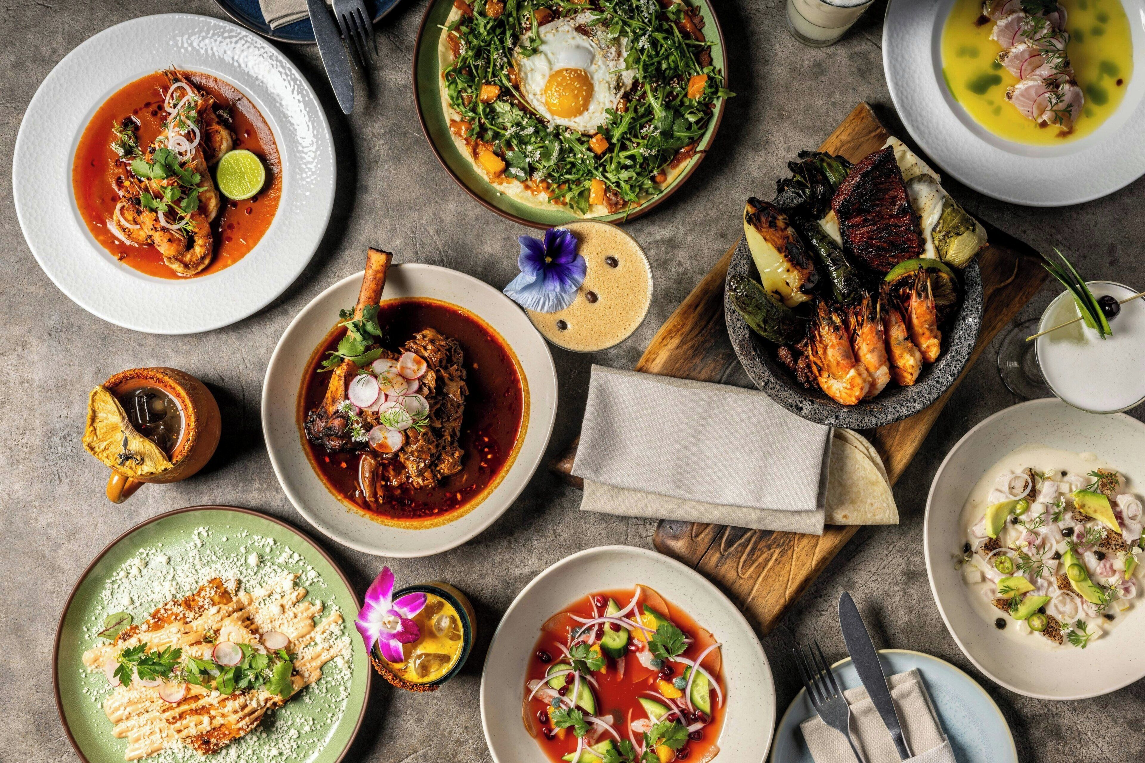 Une variété de plats sont disposés sur la table, notamment des tacos, un plat de poisson et un bol de soupe.