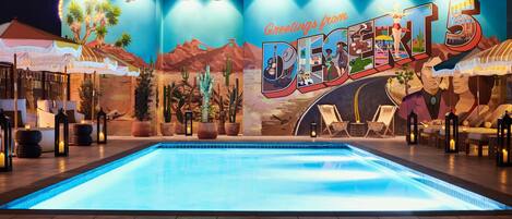A pool area with a desert-themed mural, lounge chairs, and potted plants.