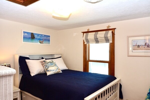 A bedroom with a bed, a window with curtains, and two framed pictures on the wall.