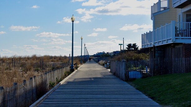 Une promenade en bois bordée de lampadaires, avec une clôture et un bâtiment doté de balcons.