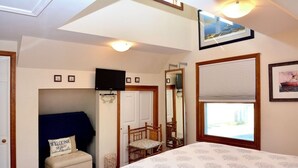 Une chambre à coucher avec un lit, une chaise, une petite table, un miroir et une fenêtre donnant sur un beau paysage.
