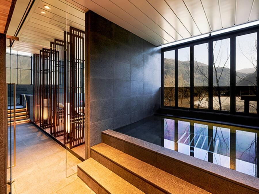 Un intérieur moderne agrémenté d’un escalier en pierre, d’une cloison en verre et offrant une vue sur un paysage montagneux.