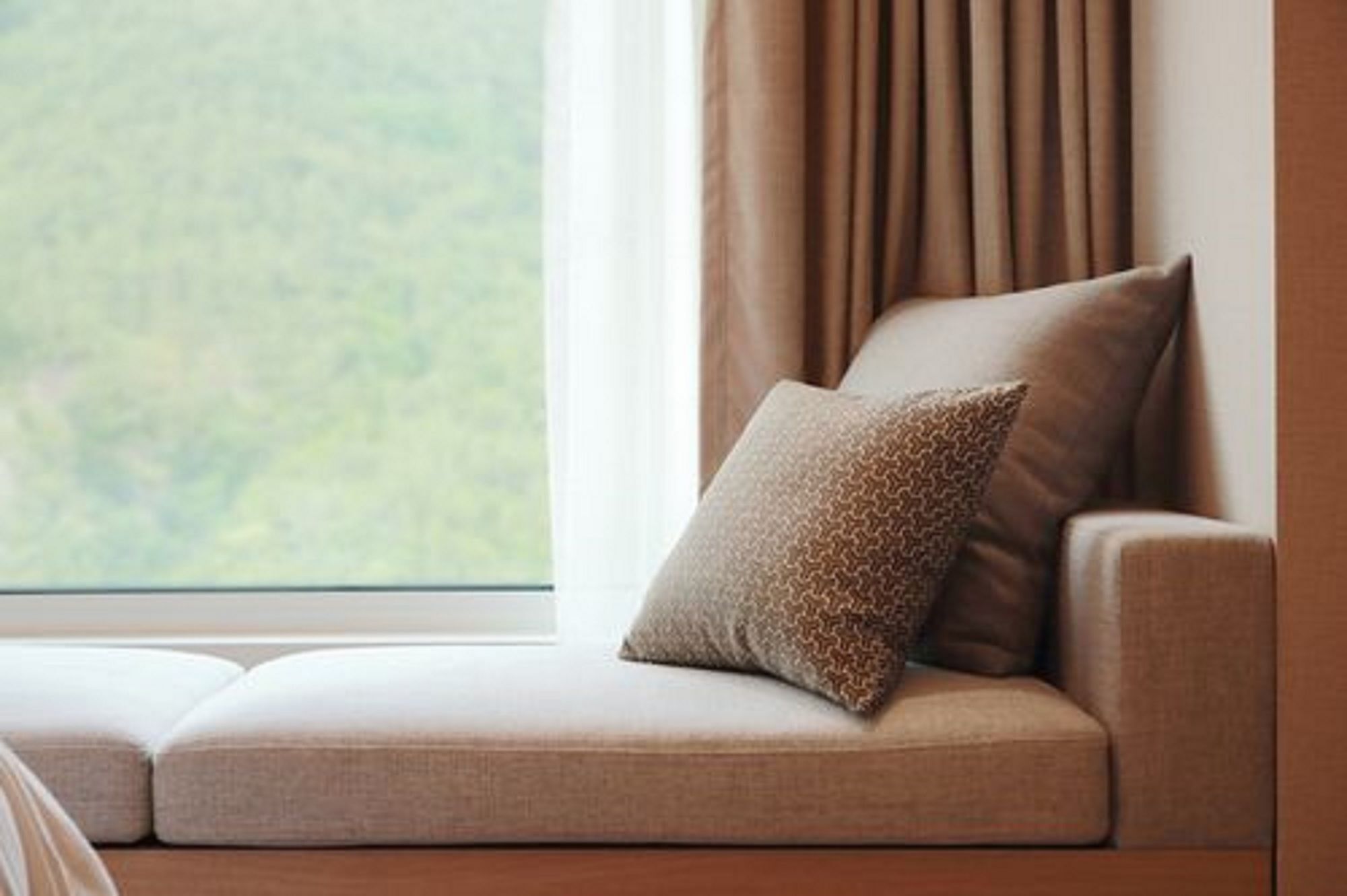 A sofa with a patterned pillow and a cushion, positioned near a window with curtains.