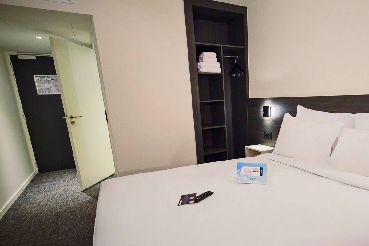 Une chambre d’hôtel avec un lit bien fait, une table de chevet avec une télécommande et une armoire contenant des serviettes pliées.