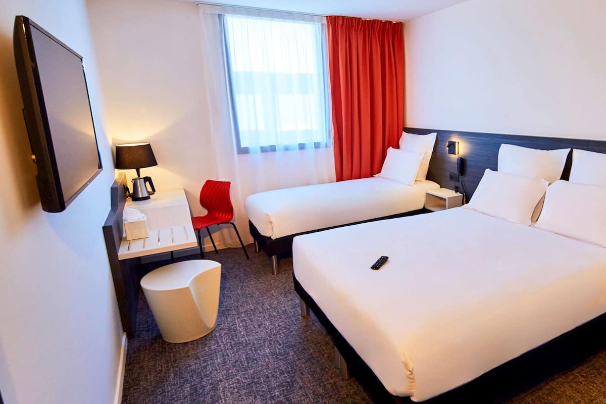 Une chambre d’hôtel avec deux lits, un bureau avec une lampe, une chaise et une petite table avec une boîte de mouchoirs.