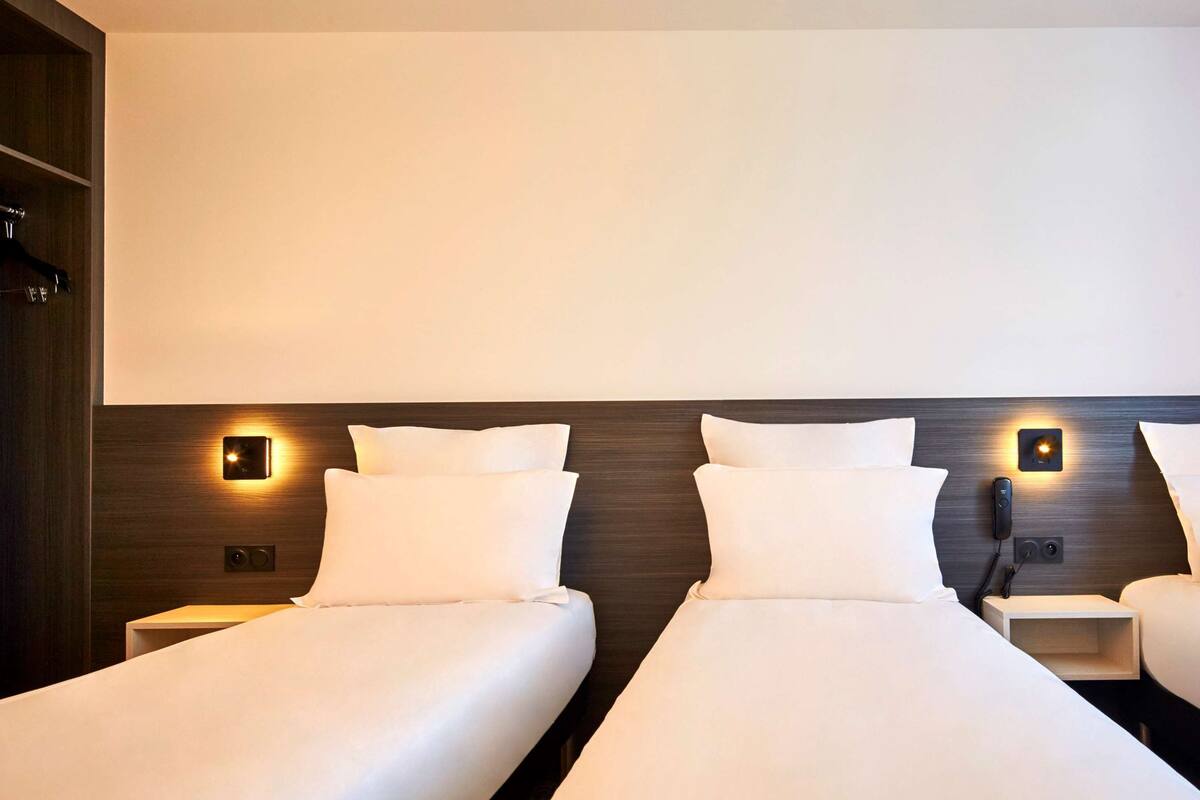 Une chambre d’hôtel avec trois lits simples, chacun étant équipé d’une table de chevet et d’une lampe fixée au mur.